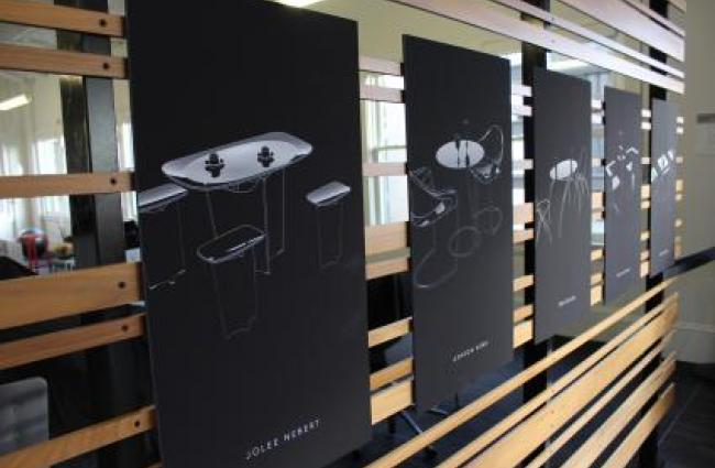 A row of student design images hung on a wood display board
